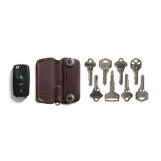 Bellroy Key Cover Plus Third Edition in brown leather with dark snaps and a car key fob alongside keys arranged on white background