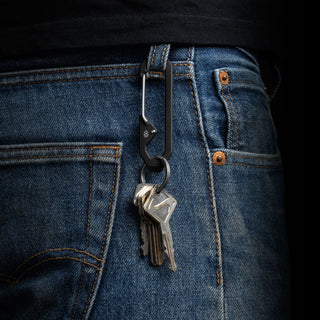 James The Holcombe Carabiner in black titanium clipped to denim jeans holding metal keys