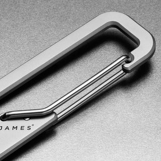 James The Holcombe Carabiner in titanium with spring-loaded latch on a textured gray surface