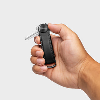 Hand holding black leather Orbitkey Key Organizer Pro Leather compact key holder with one key attached