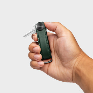 Orbitkey Key Organizer Pro Leather in dark green held in hand with a single key attached and black hardware