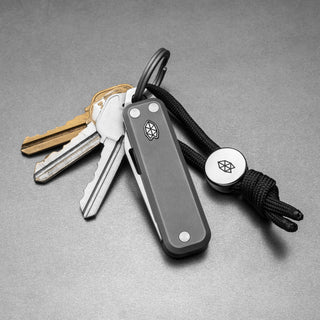 James The Elko Knife in gray titanium with a black cord attached to a keyring and keys