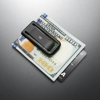 James The Martindale Money Clip in black titanium holding cash and cards on a dark surface