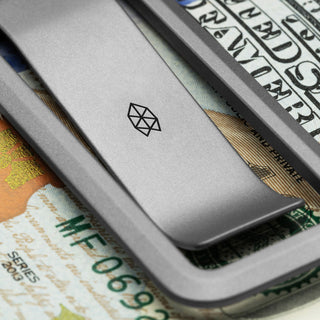 James The Martindale Money Clip in titanium holding US dollar bills with matte finish and logo shown