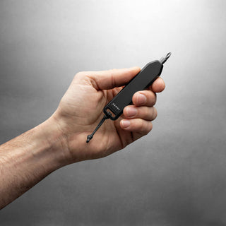 Hand holding black anodized aluminum James The Warrick Bit Driver with nylon lanyard against gray background