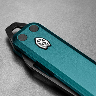 James The Elko Knife with textured teal aluminum handle and distinctive geometric logo close-up