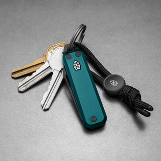 James The Elko Knife in teal with black lanyard attached to keyring holding three keys on gray surface