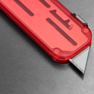 James The Palmer Recycled PC Knife with translucent red recycled PCTG handle and sharp utility blade angled on gray surface