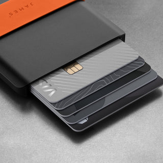 James The Lowe Wallet showcasing black aluminum casing with silicone band and cards fanned out on gray surface