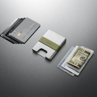 James The Lowe Wallet in aluminum with olive silicone band holding cards and cash flat on gray surface