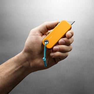 Hand holding James The Palmer Knife with bright orange anodized aluminum handle and exposed blade