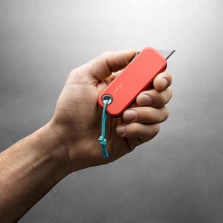 Hand holding James The Palmer Knife with red anodized aluminum handle and blue lanyard cord