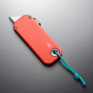 James The Palmer Knife with anodized red aluminum handle and blue lanyard on gray surface