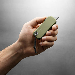 Hand holding olive green James The Palmer Knife with exposed utility blade and lanyard loop
