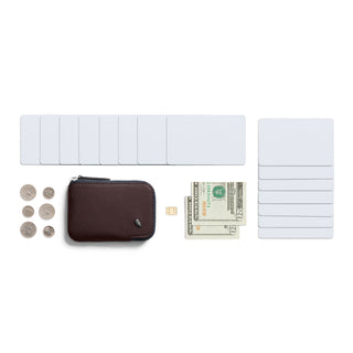 Bellroy Card Pocket in dark leather with coins, cards, cash, and SIM card on white background