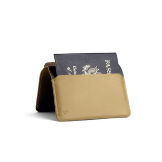 Bellroy Passport Cover in tan leather holding a black passport at an angled view on white background