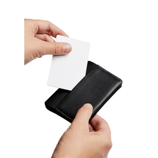 Bellroy Under Cover black leather card holder with a hand inserting a white card into the slot