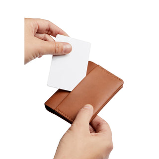 Bellroy Under Cover card holder in tan leather with hands inserting a white card gently