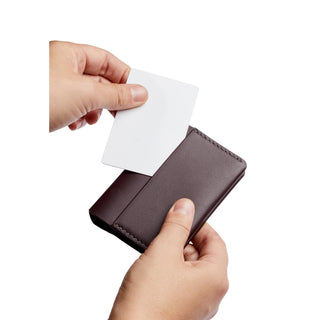 Bellroy Under Cover slim brown leather card holder showing card insertion in hand close-up