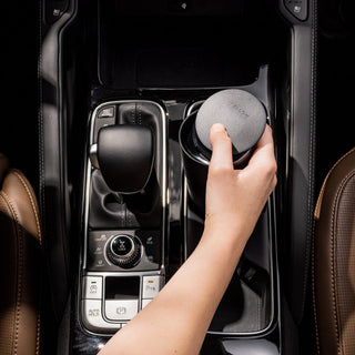 Hand holding FELLOW Carter Slide Mug 12oz with textured gray lid inside a car cup holder next to gear shift