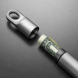 James The Randolph Capsule titanium container with threaded cap storing rolled cash on gray background