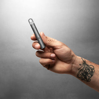 Hand holding James The Randolph Capsule in matte titanium with smooth CNC-machined finish by The James Brand