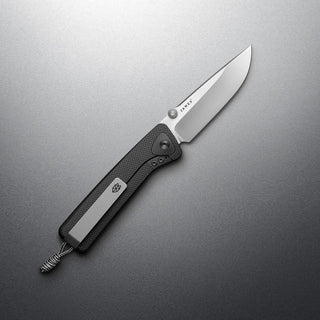 James The Barnes Knife with textured black handle and polished Böhler M390 stainless steel blade angled on gray surface