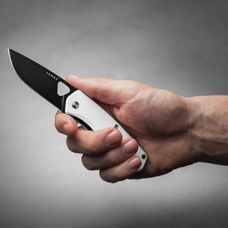 James The Folsom Knife with black blade and white textured handle held in hand against gray background