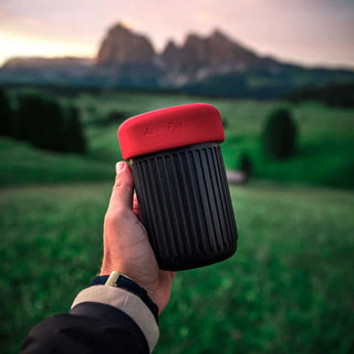 AeroPress Go Coffee Maker with red lid and black ribbed body held outdoors at sunset