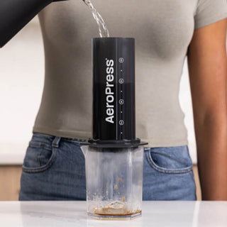AeroPress Carafe in use pouring water through black Tritan™ hexagonal coffee brewer on white surface