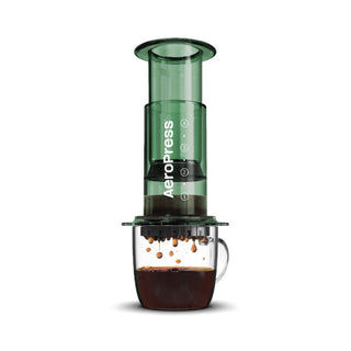 AeroPress Clear Coffee Maker brewing fresh coffee into a clear glass mug with visible coffee droplets