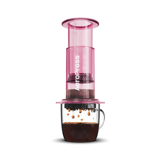 AeroPress Clear Coffee Maker in pink plastic brewing fresh coffee into clear glass mug