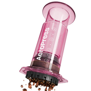 AeroPress Clear Coffee Maker in translucent pink releasing brewed coffee grounds from filter cap