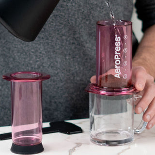 AeroPress Clear Coffee Maker with translucent purple brewing chamber over glass mug on marble surface