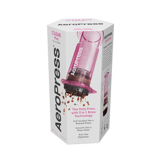 AeroPress Clear Coffee Maker in translucent pink releasing coffee grounds from the bottom filter section