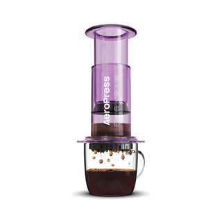 AeroPress Clear Coffee Maker brewing dark coffee with purple translucent chamber over glass mug
