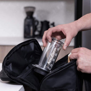 A person placing the AeroPress Clear Coffee Maker into a black carrying bag on a kitchen counter