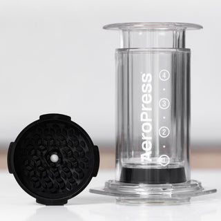 AeroPress Clear Coffee Maker showing its transparent chamber and black filter cap with honeycomb pattern