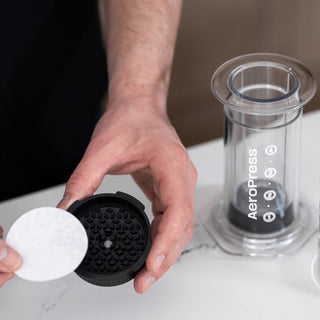 AeroPress Clear Coffee Maker with clear chamber and filter cap held over white surface
