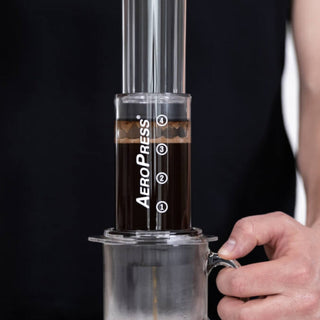 AeroPress Flow Control Filter Cap attached to AeroPress brewing device with coffee dripping into glass mug