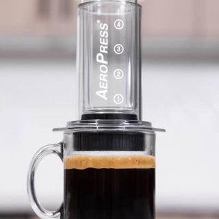 AeroPress Flow Control Filter Cap attached to AeroPress brewing fresh coffee in clear glass mug