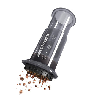 AeroPress Go Coffee Maker made of transparent plastic with ground coffee spilling from the bottom filter