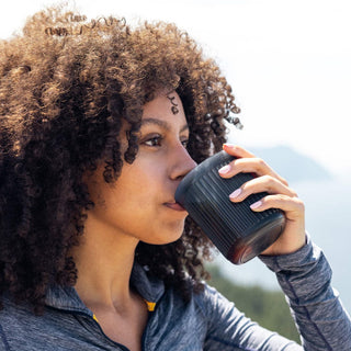 Woman drinking coffee from black AeroPress Go Coffee Maker cup outdoors with a scenic background