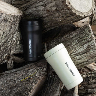 AeroPress Go Plus Travel System in black and white on rustic wood logs background