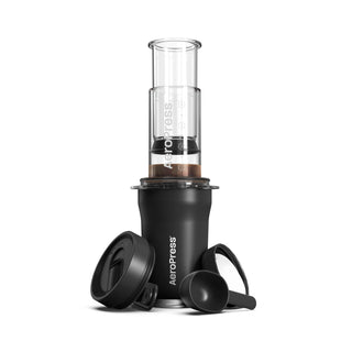 AeroPress Go Plus Travel System black coffee maker with clear chamber, lid, and black scoop on white background