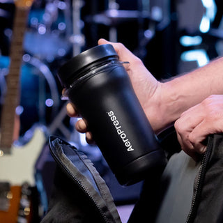 A hand holding AeroPress Go Plus Travel System black stainless steel coffee maker cup