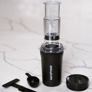 AeroPress Go Plus Travel System compact coffee maker with black cup and clear brewing chamber on marble surface