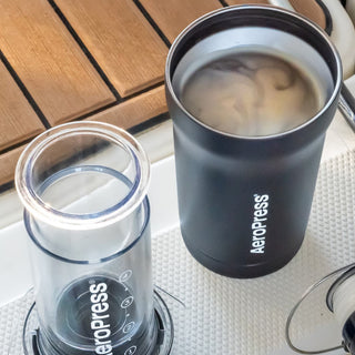 AeroPress Go Plus Travel System black mug with swirling coffee and clear brewing chamber on tray surface