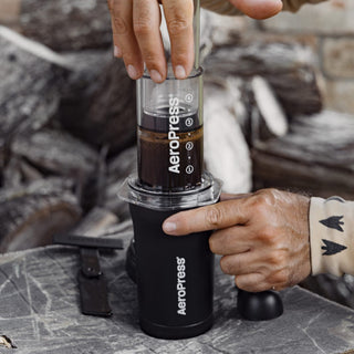 AeroPress Go Plus Travel System brewing coffee outdoors with black compact design and clear chamber