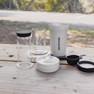 AeroPress Go Plus Travel System with clear brewing chamber and white reusable travel mug outdoors